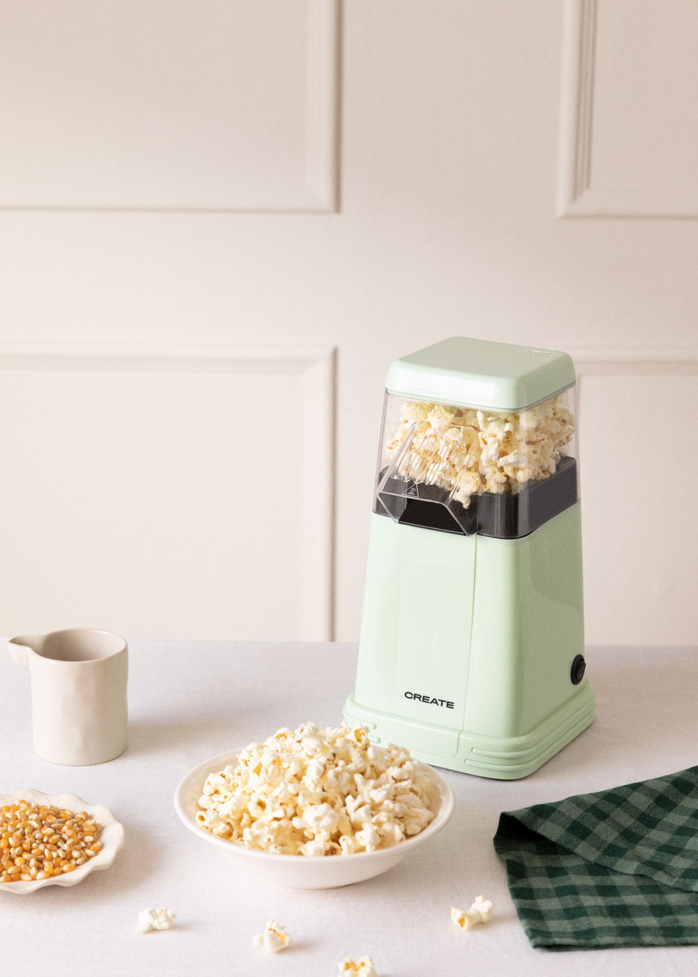 Máquina de palomitas verde con palomitas, granos y un tazón de palomitas.