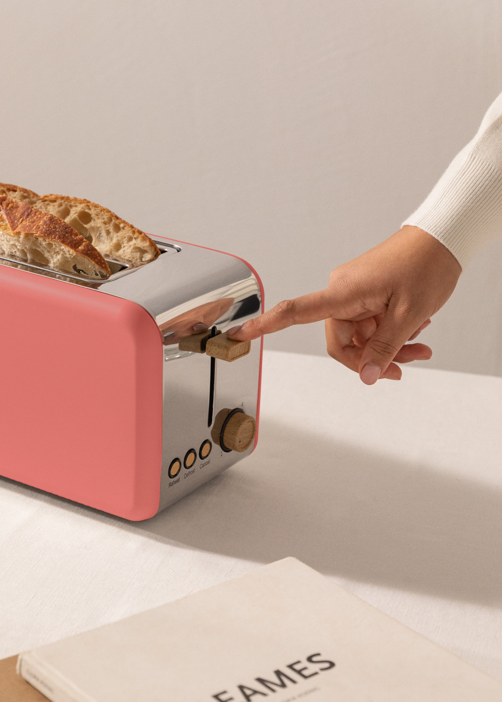 Una tostadora rosa con pan dentro. Una mano está presionando la palanca.