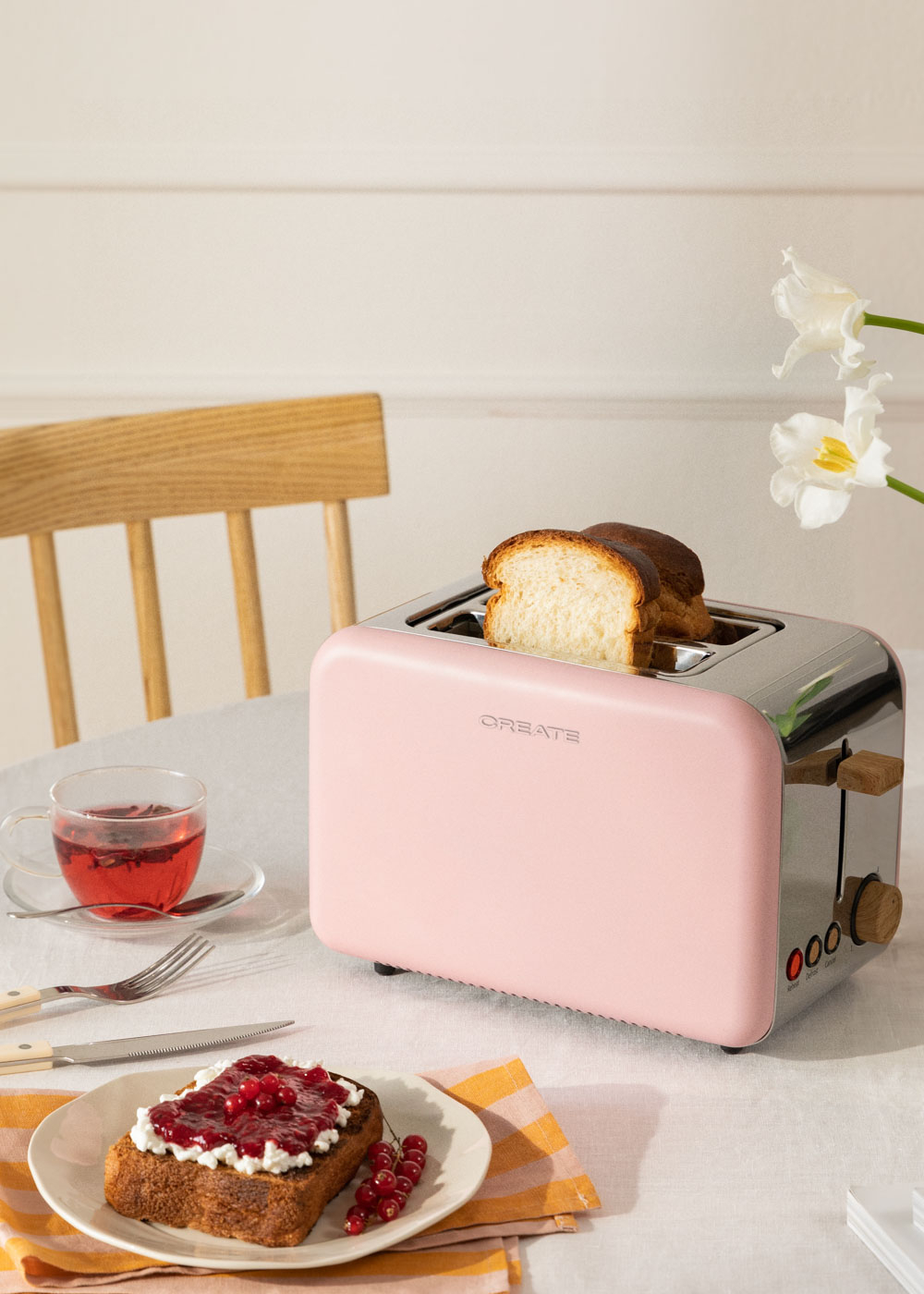 Una tostadora rosa con pan dentro y una tostada con mermelada. Una taza de té en la mesa.