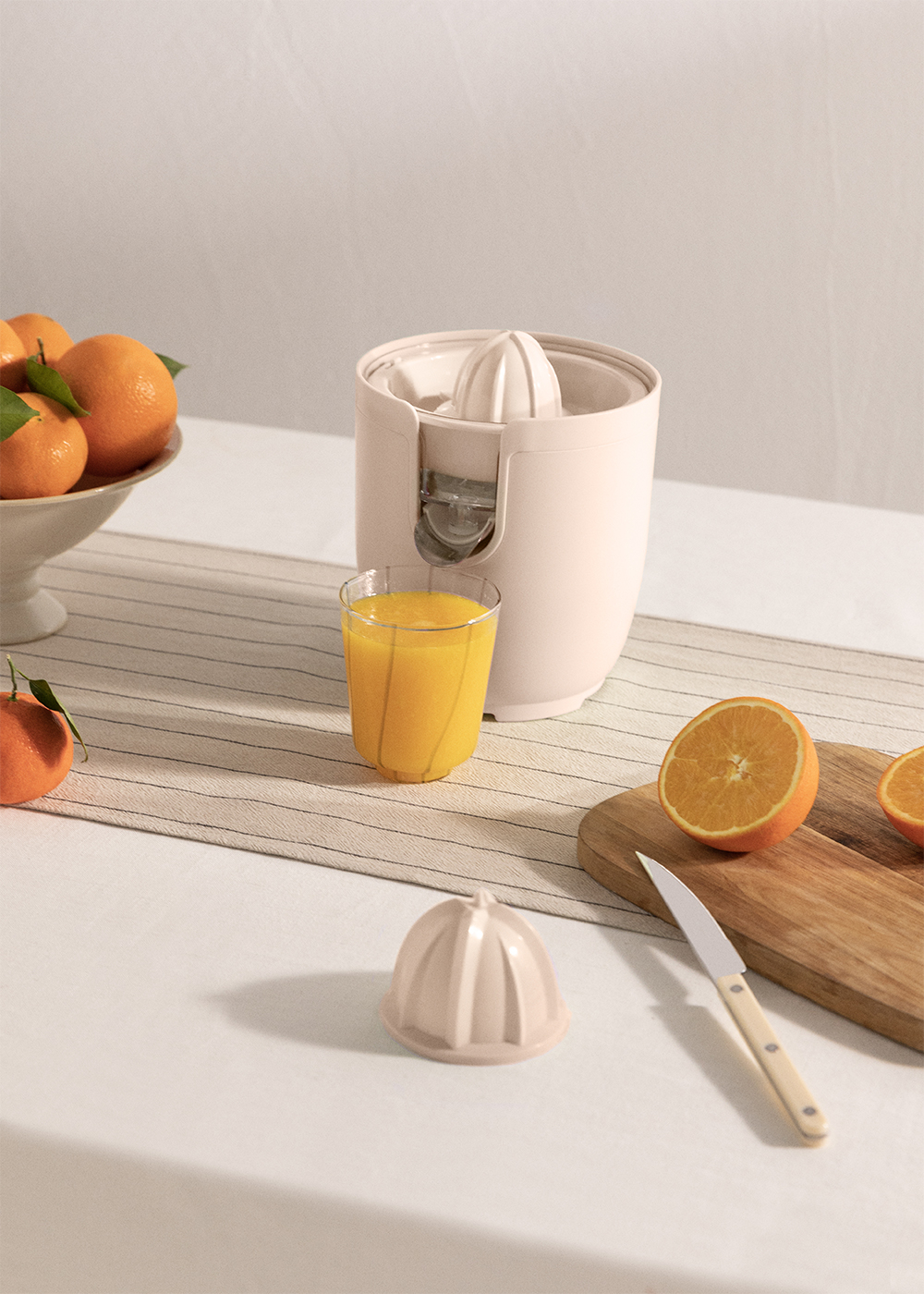 Exprimidor blanco con naranjas y un vaso de zumo. Un cuchillo y media naranja.