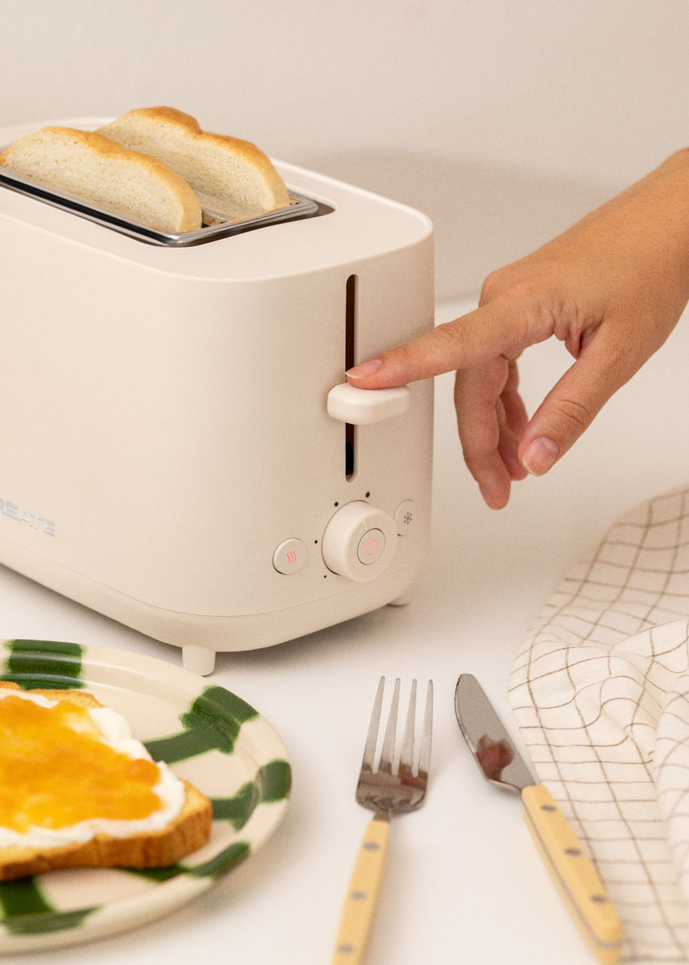 La main d'une personne réglant un grille-pain. Il y a du pain et une assiette avec de la marmelade.