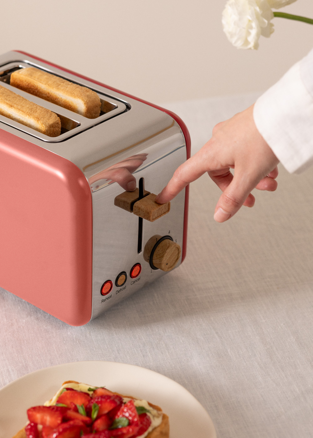 Una mano está presionando un botón en una tostadora rosa. Hay dos rebanadas de tostadas dentro.
