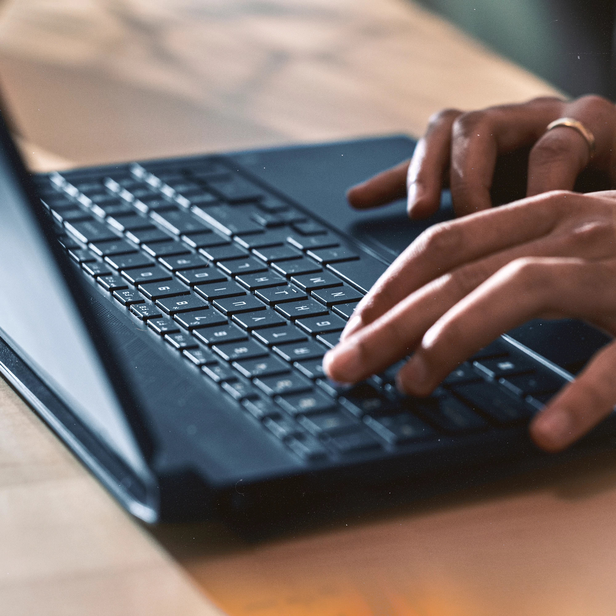 Ręce piszące na czarnej klawiaturze laptopa na drewnianym stole.