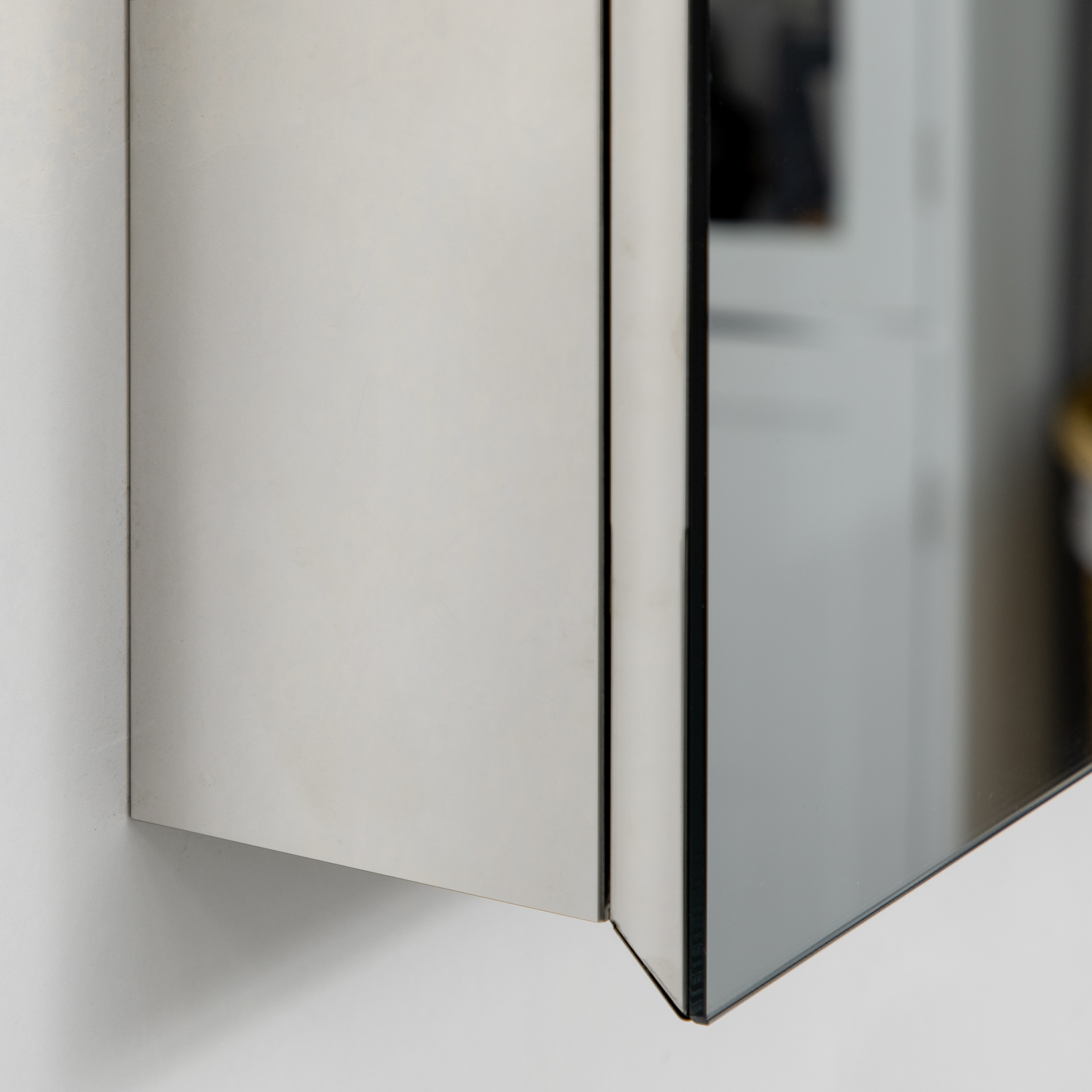 Nahaufnahme eines metallischen Schranks. Die Spiegeltür ist teilweise geöffnet und reflektiert eine weiße Wand.