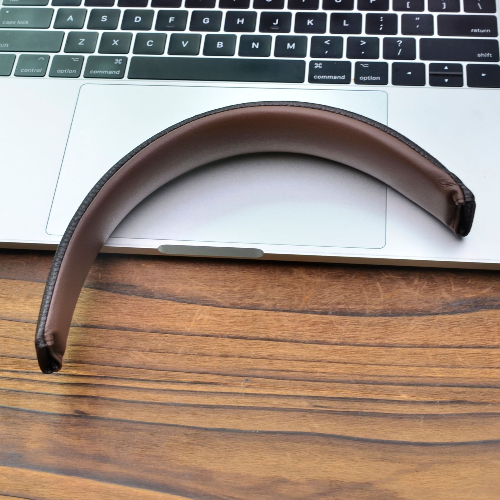 Un cuscino poggiatesta in pelle marrone sulla tastiera e sul trackpad di un MacBook. Superficie in legno sottostante.