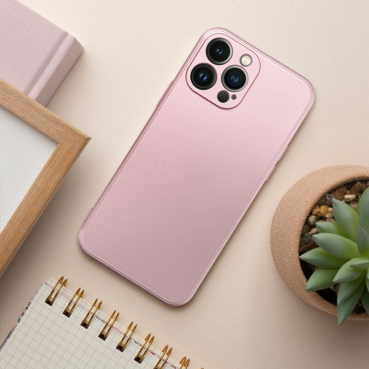 Ein pinkfarbenes Smartphone mit Hülle, mit Notizbuch, Stift und Pflanze auf dem Tisch.