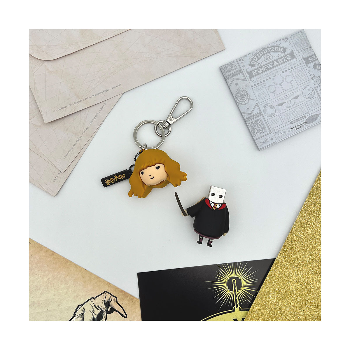Porte-clés et clé USB sur le thème d'Harry Potter sur une surface blanche avec enveloppes et livre.