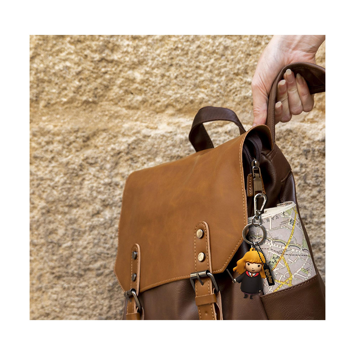 Une personne tient un sac à dos marron avec un porte-clés. Le sac est marron avec une carte à l'intérieur.