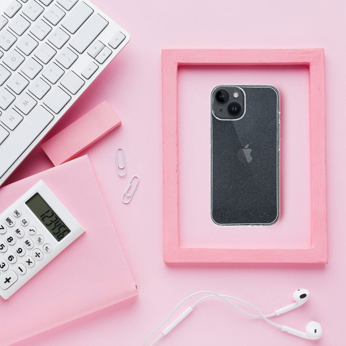 Ein rosa Schreibtisch-Setup mit einem Telefon in einem rosa Rahmen, Tastatur, Taschenrechner, Kopfhörern und Büroklammern.
