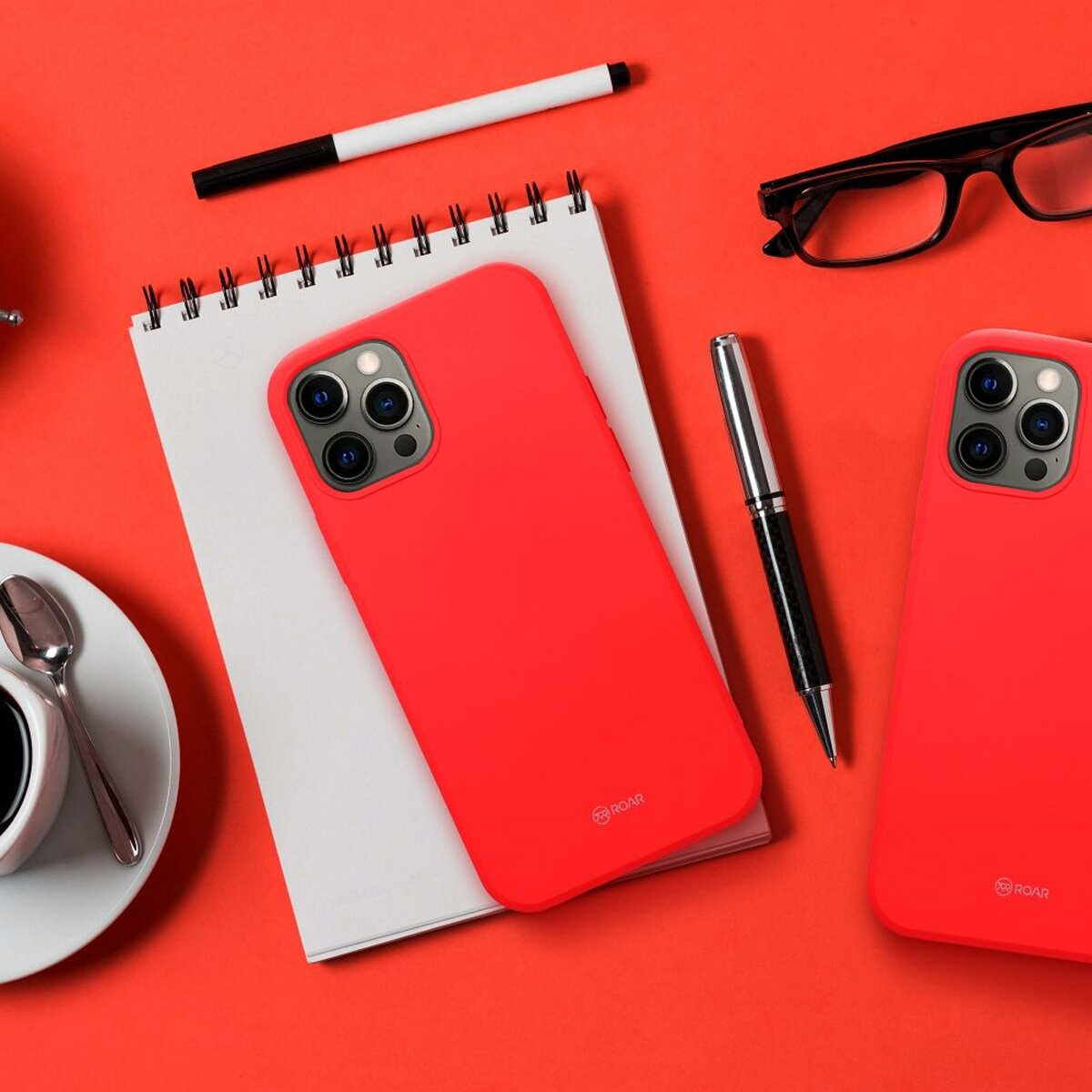 Rote Handyhüllen, Stift, Notizbuch und Brille auf roter Oberfläche. Kaffeetasse und Löffel.