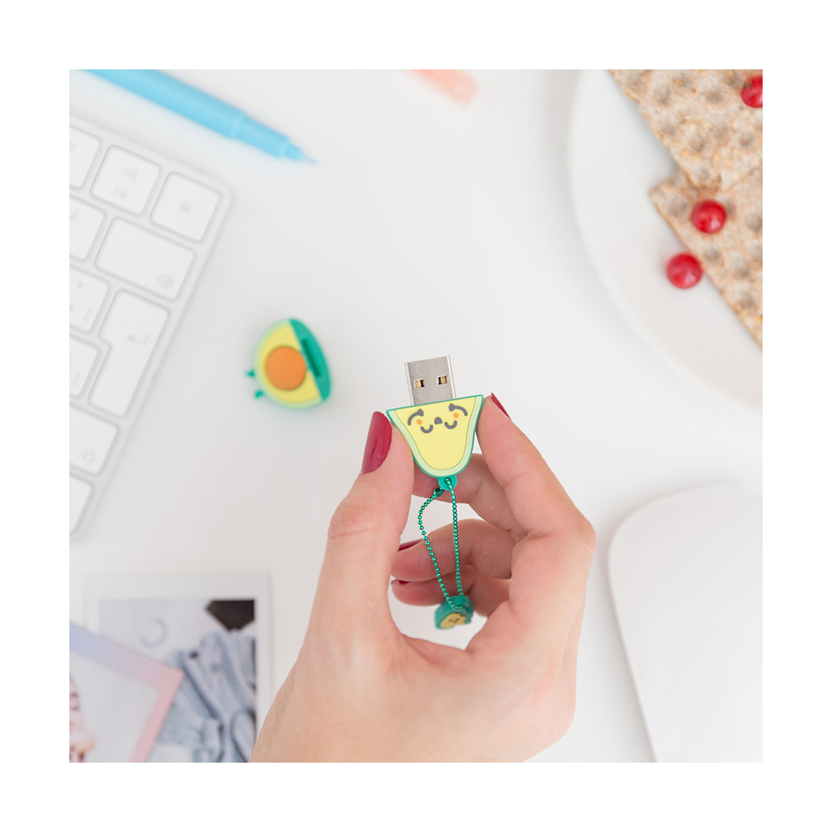 Eine Person hält einen USB-Stick in Form einer Avocado, mit Tastatur und Maus im Hintergrund.