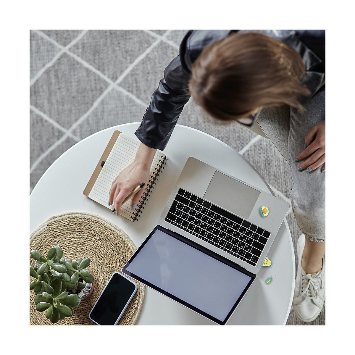 Draufsicht: Hände einer Person auf einem Laptop und einem Notizbuch, mit Telefon, Pflanze und Kaffee.