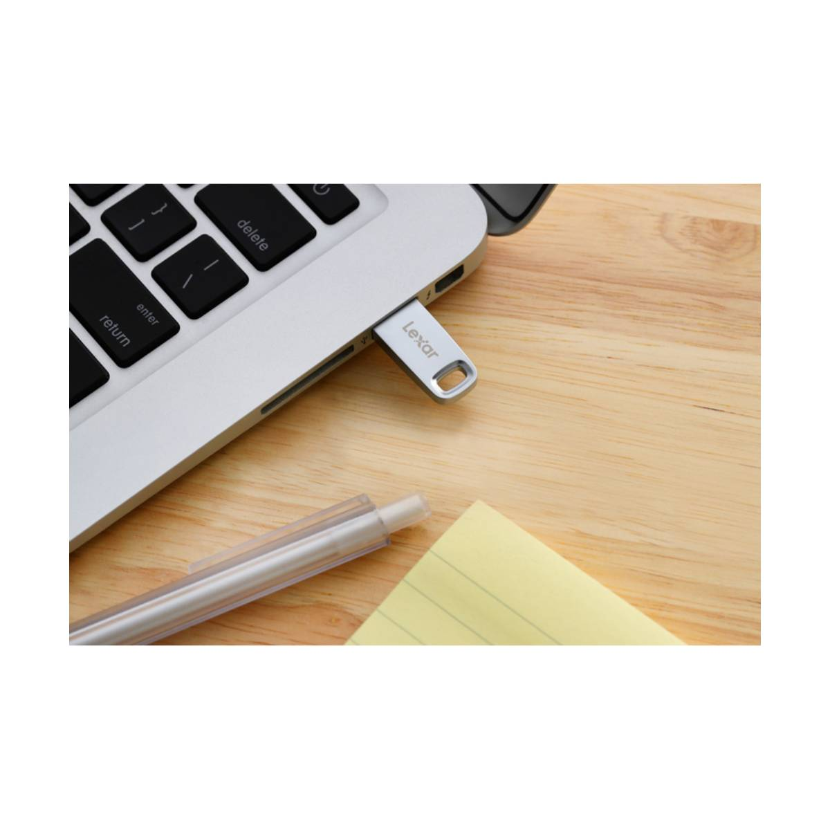 Un'unità flash USB Lexar argentata collegata a un laptop, vicino a un post-it giallo.