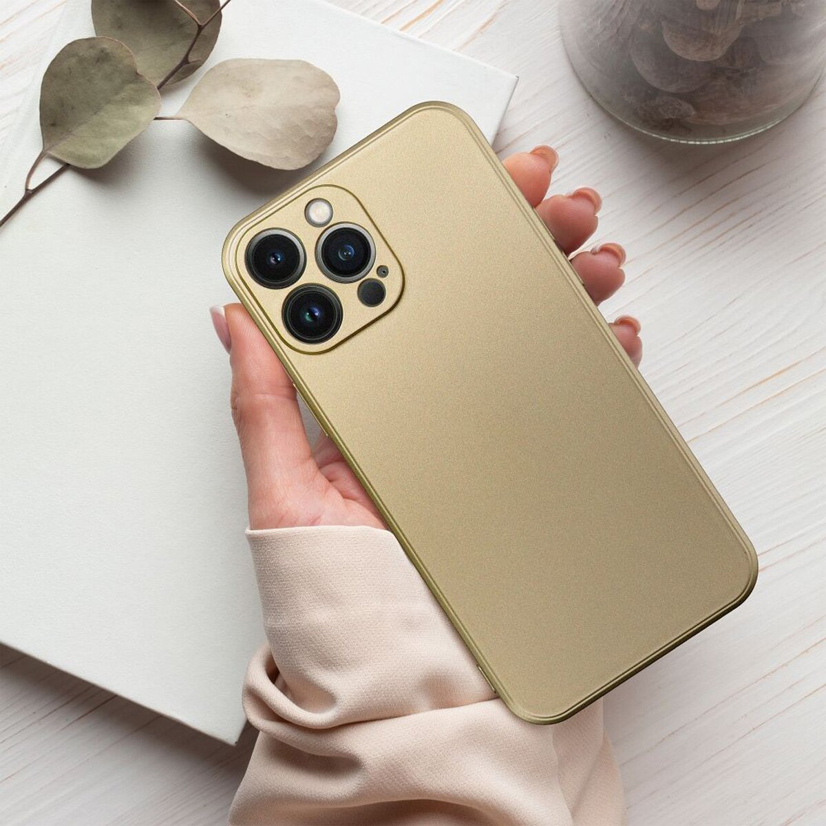 Ein goldenes Telefon mit drei Rückkameras in einer Hand, auf weißem Hintergrund.