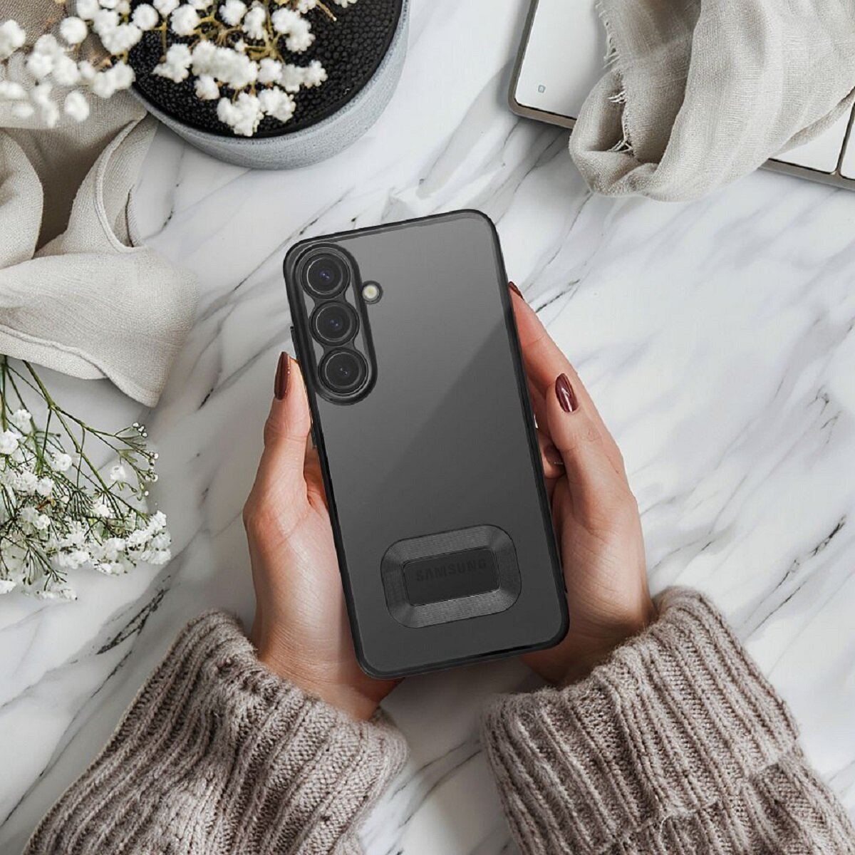 Hände halten ein schwarzes Telefon mit schwarzem Gehäuse auf einer Marmoroberfläche.