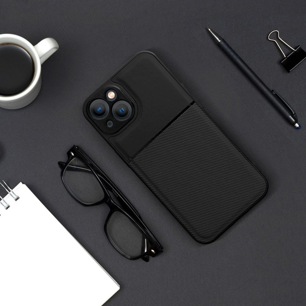 Eine schwarze Handyhülle mit schwarzem und Karbonfaser-Design, ein Notizblock, Brille, Stift und Kaffeetasse.