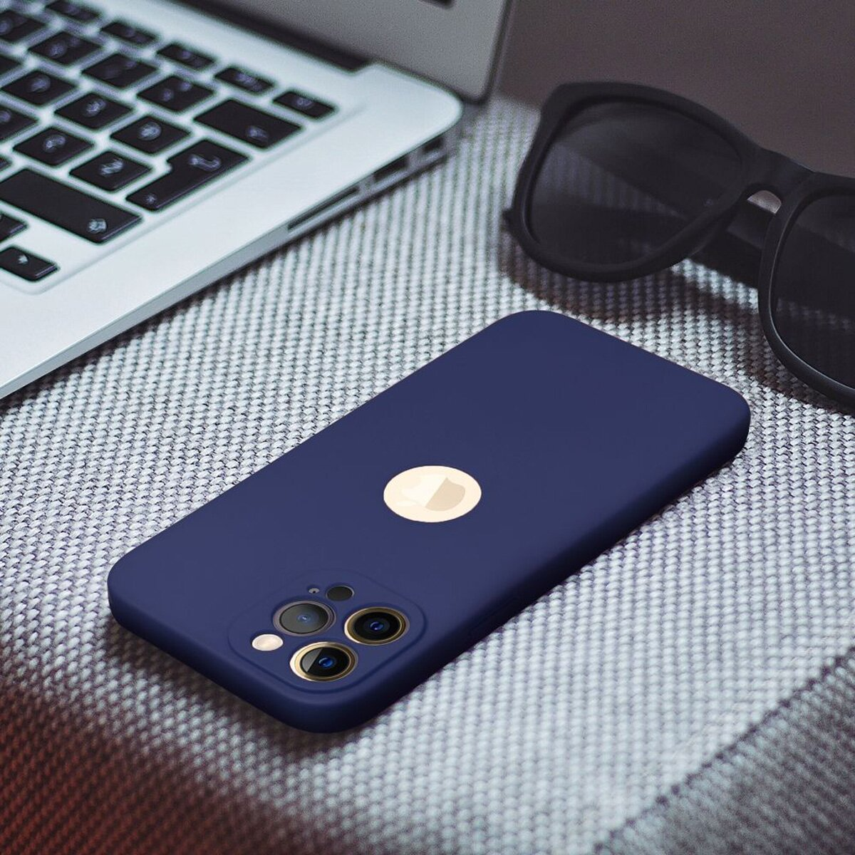 Eine marineblaue Handyhülle mit einem goldenen Apple-Logo, liegt auf einer strukturierten Oberfläche mit einem Laptop.