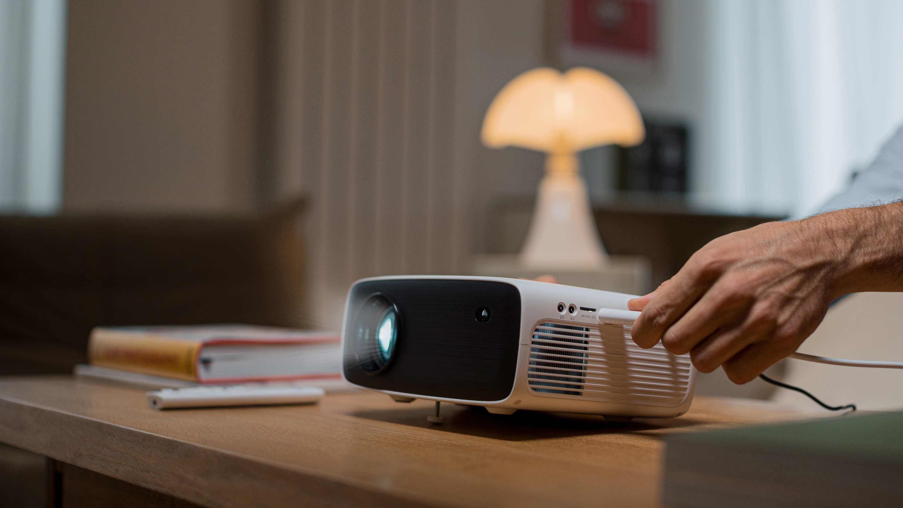 Biały projektor na drewnianym stole z ręką osoby podłączającej kabel.