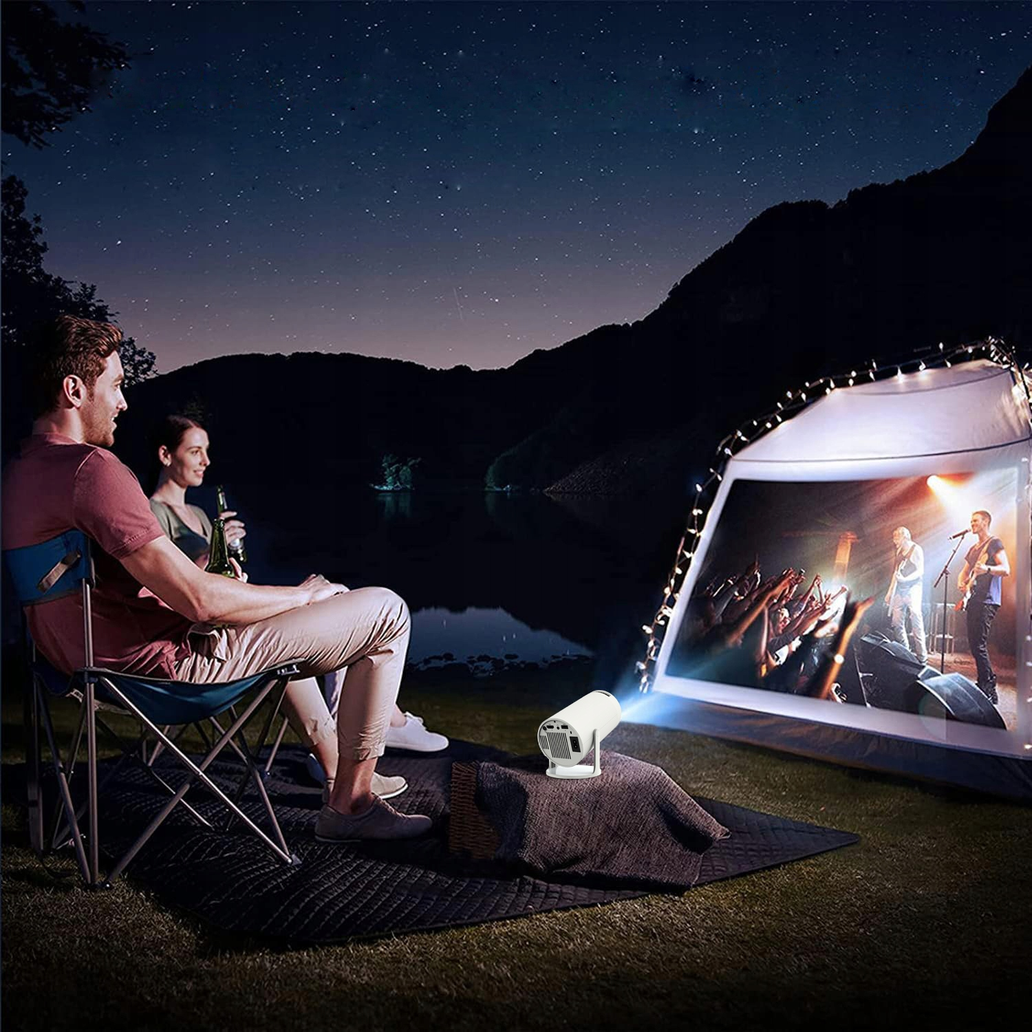 Para ogląda film wyświetlany na namiocie w nocy. Projektor stoi na macie.