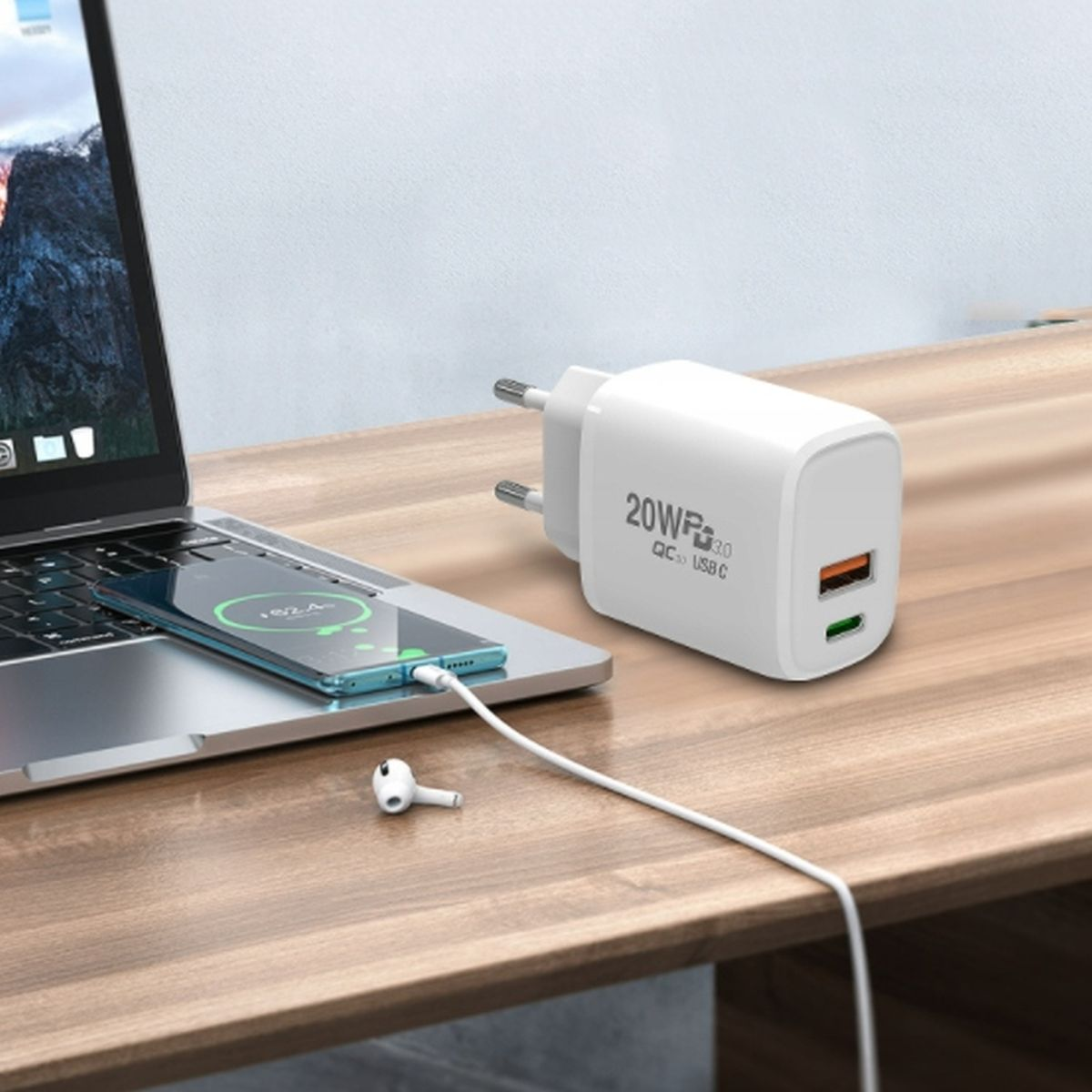 Biała ładowarka podłączona do laptopa, ładująca telefon. Słuchawka leży obok na drewnianym stole.