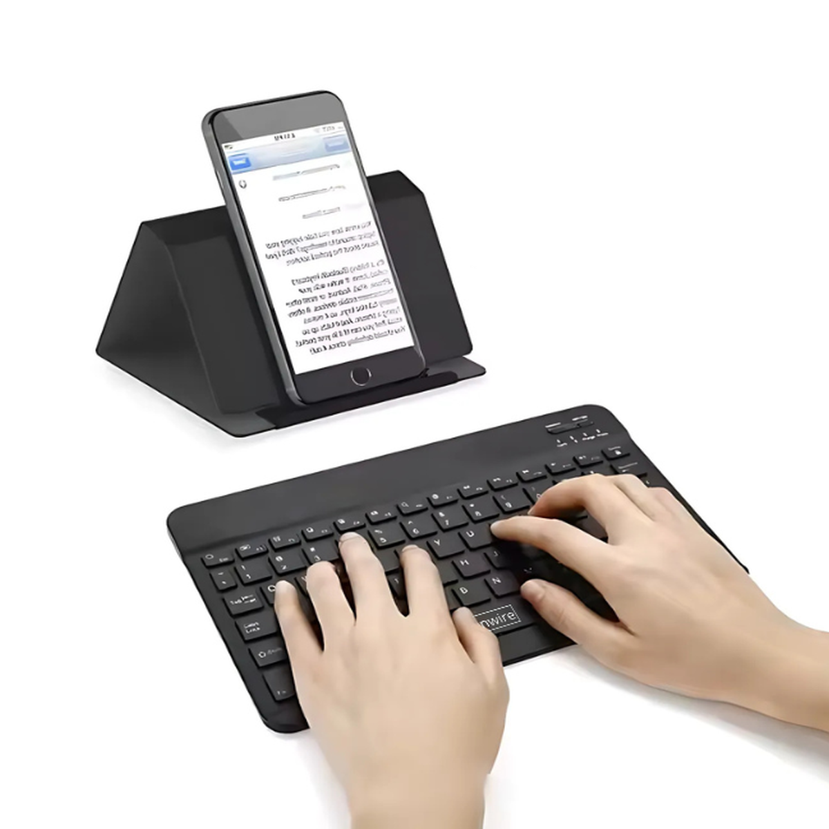 Dłonie piszące na czarnej klawiaturze. Telefon na stojaku, wyświetlający tekst. Nowoczesna konfiguracja biurka.