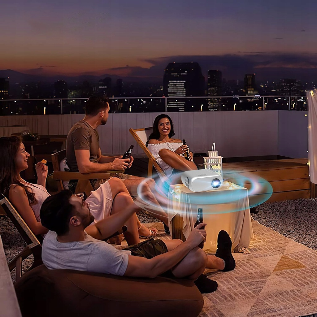 Ludzie oglądający film na dachu z projektorem. Scena nocna, tło miasta.