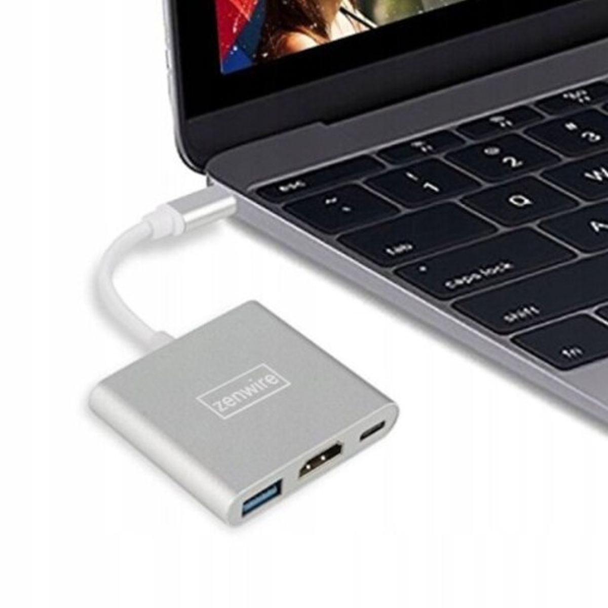 Srebrny adapter z portami HDMI i USB jest podłączony do laptopa. Adapter znajduje się na białej powierzchni.