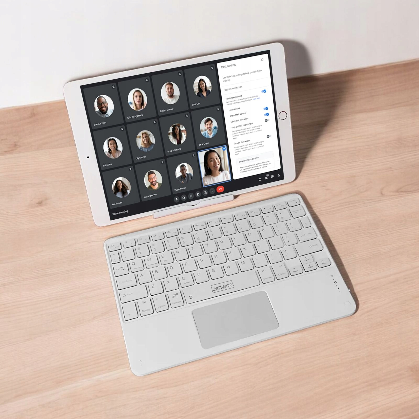 Tablet na stojaku z wideorozmową, biała klawiatura na drewnianym stole.