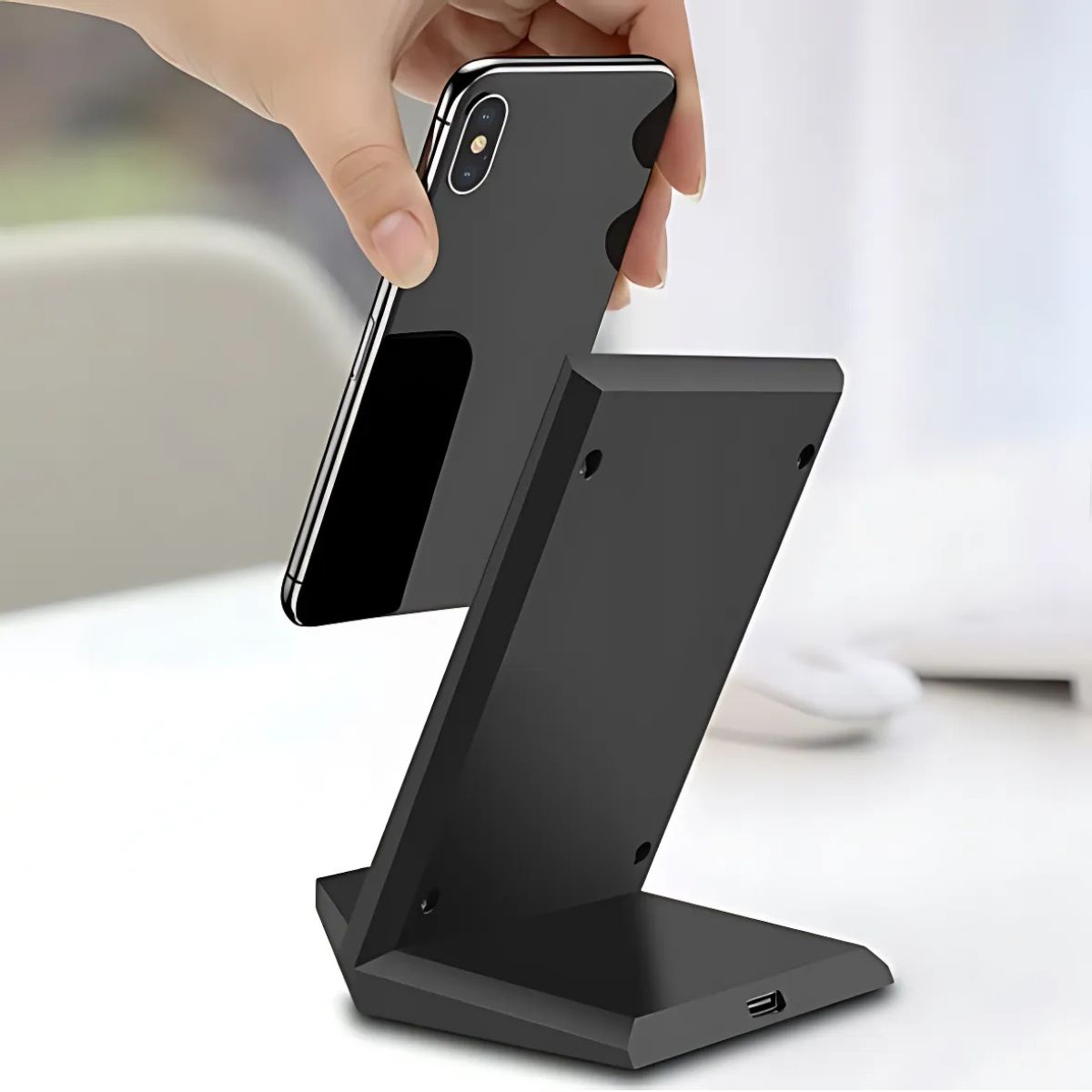 Ręka umieszczająca czarny telefon na czarnej, pochylonej ładowarce bezprzewodowej.