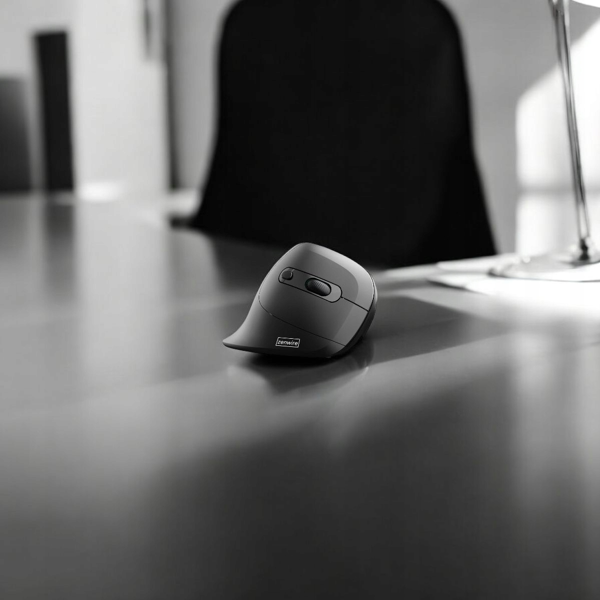 Ciemnoszara ergonomiczna mysz na czarnym biurku, ze światłem z prawej strony.