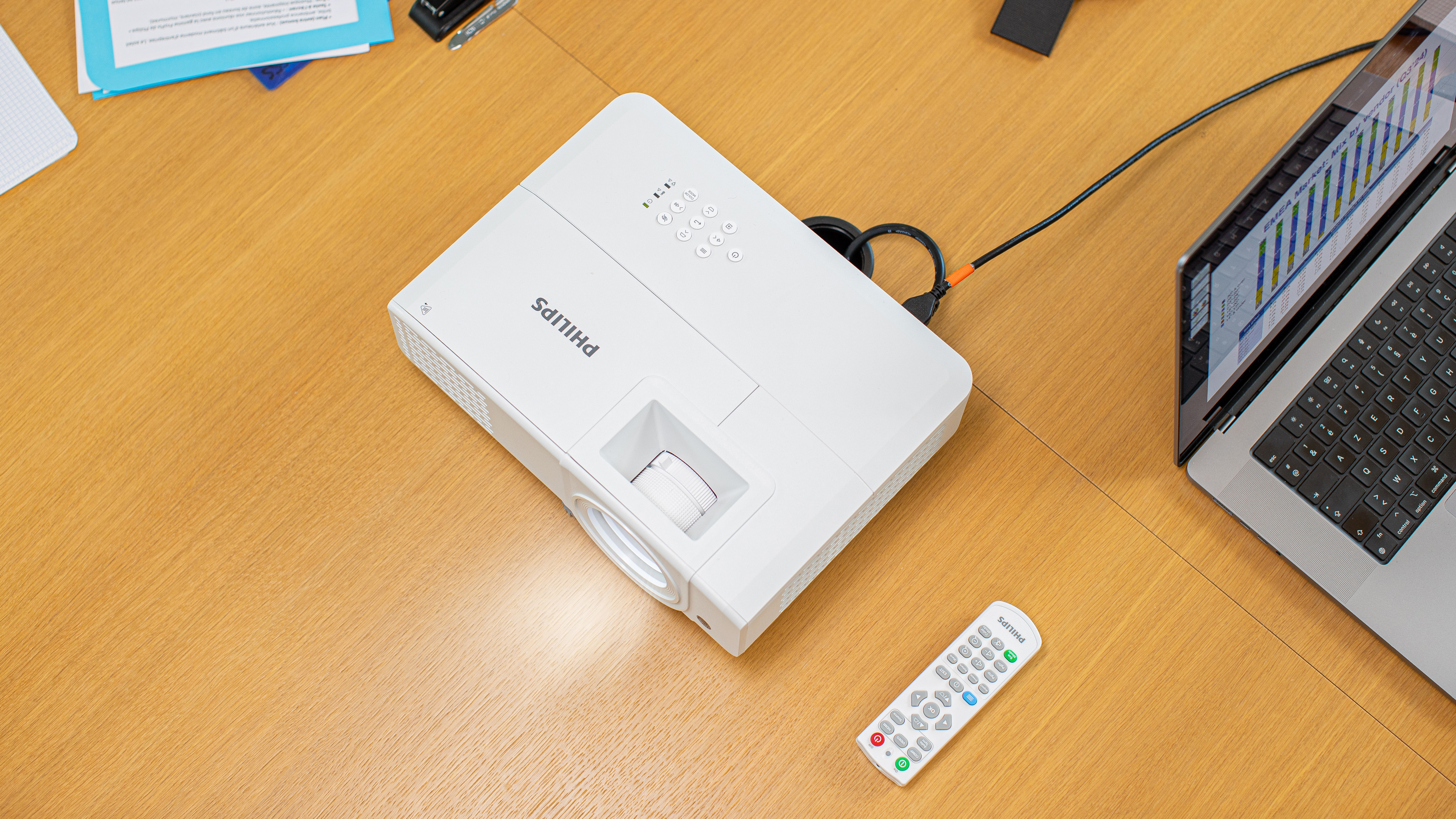 Witte Philips projector op houten tafel. Afstandsbediening en laptop zijn ook aanwezig.