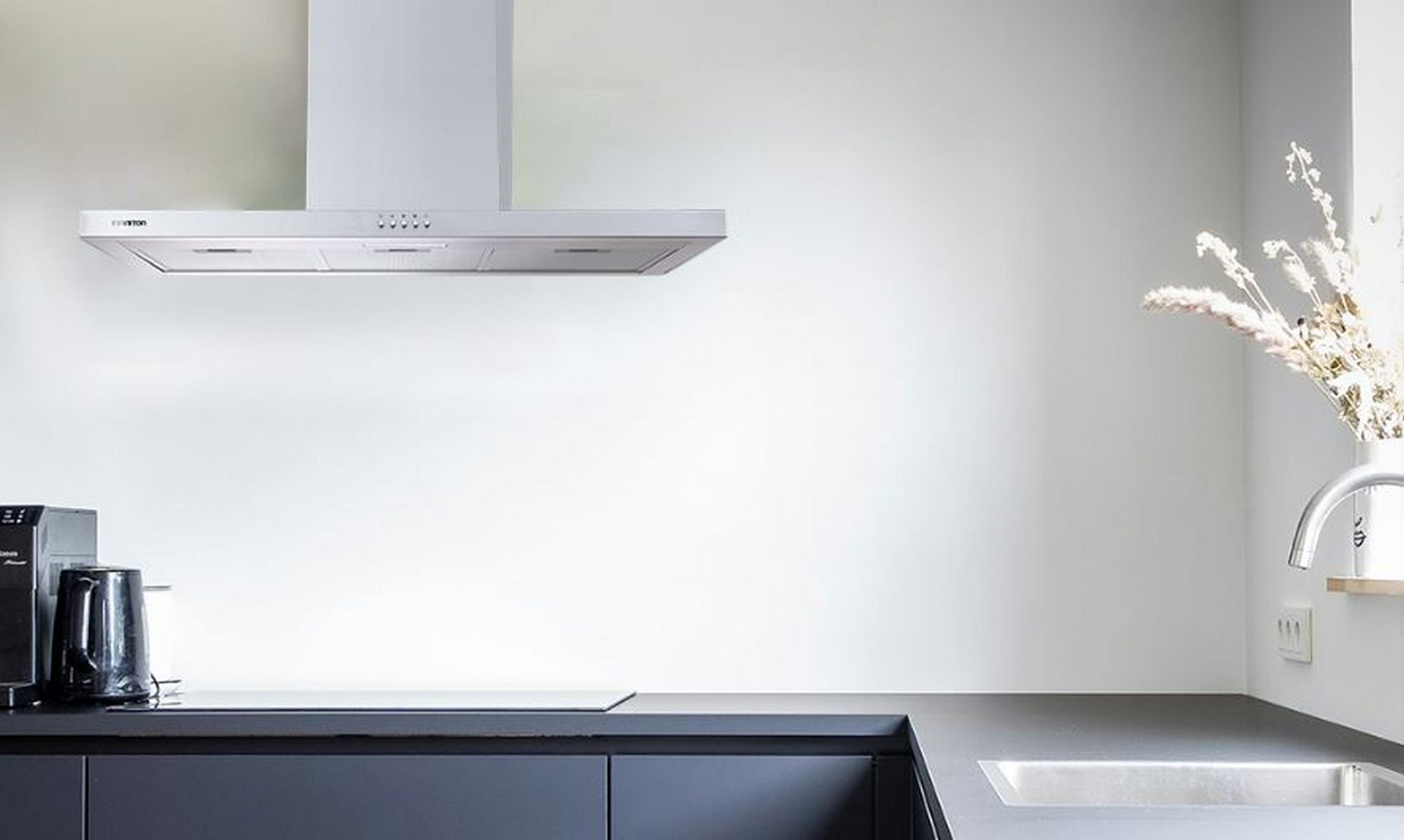 Una cocina con campana extractora de acero inoxidable, encimera, fregadero y cafetera negra.
