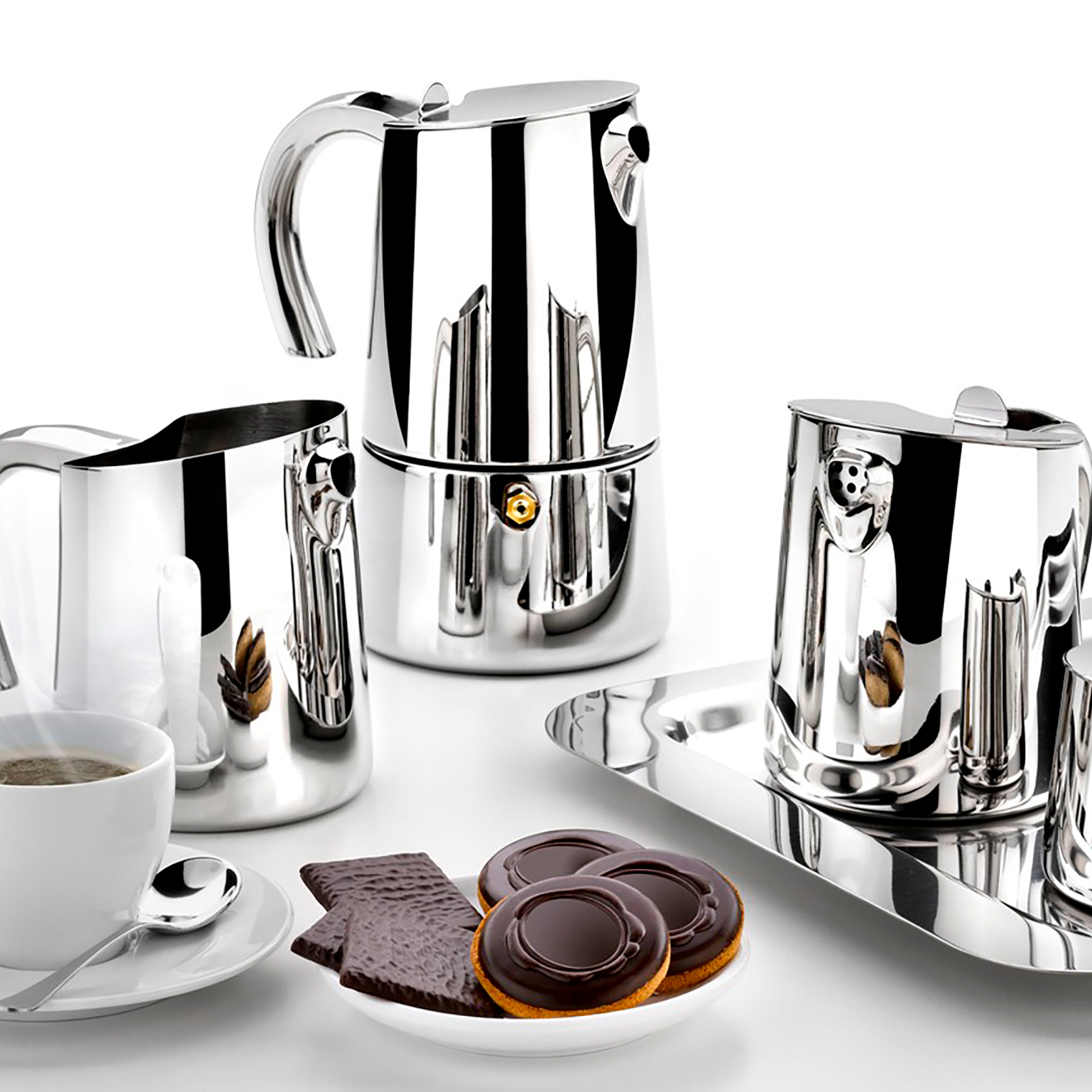 Błyszczący chromowany zestaw do kawy z filiżanką kawy i ciastkami na białej powierzchni.