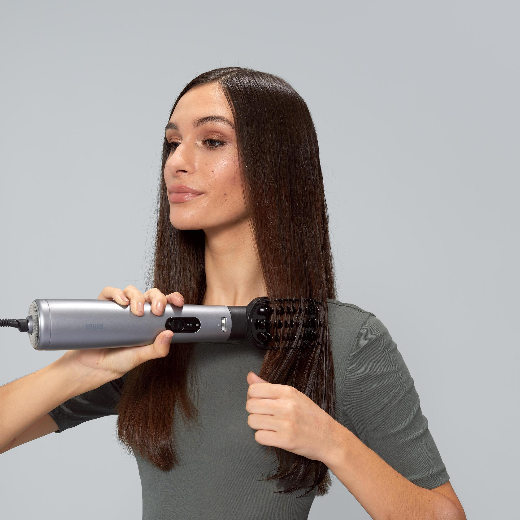 Donna che si acconcia i capelli con un arricciacapelli. Sfondo grigio.