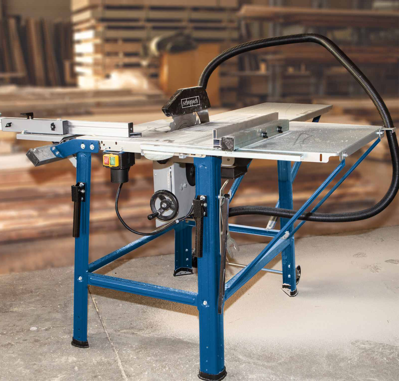 Tafelzaagmachine, blauw frame, op een houten vloer, in een werkplaats, met een zwarte slang bevestigd.