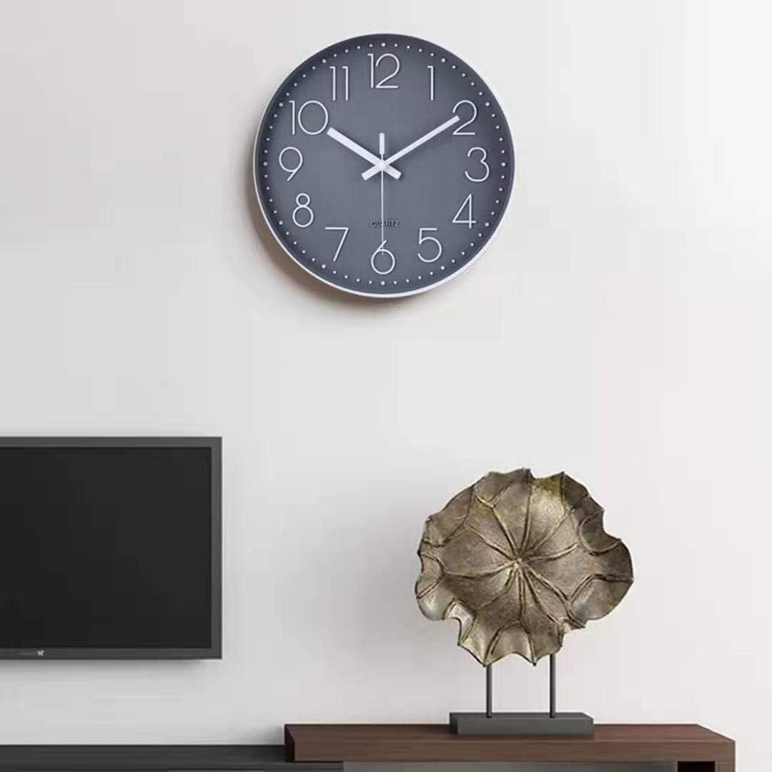 Graue Uhr mit weißen Zeigern und Zahlen, an einer weißen Wand, mit Dekoration.
