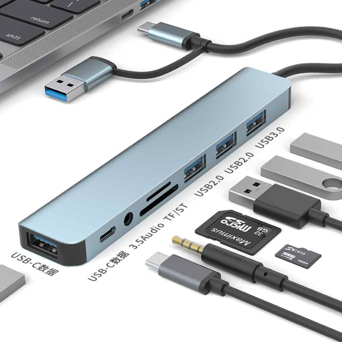 Ein Laptop mit USB-Hub, Kabeln und angeschlossenem Zubehör auf weißer Oberfläche.