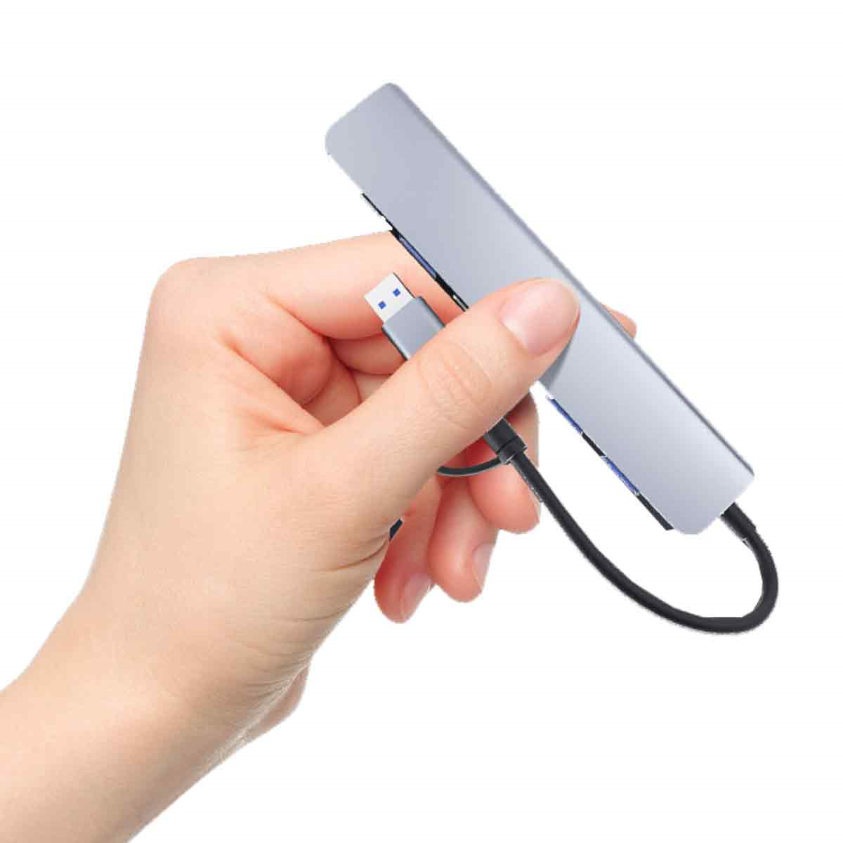 Eine Hand hält einen silbernen USB-Hub mit mehreren Anschlüssen und einem schwarzen USB-Kabel.
