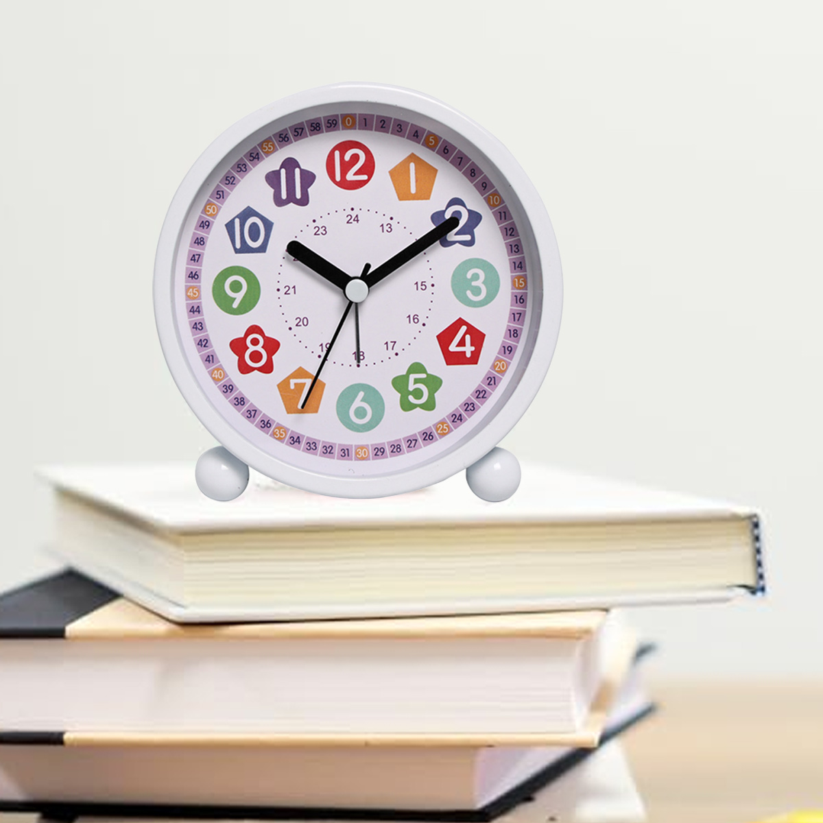Weißer analoger Wecker mit bunten Zahlen und Zeigern, der auf Büchern liegt.