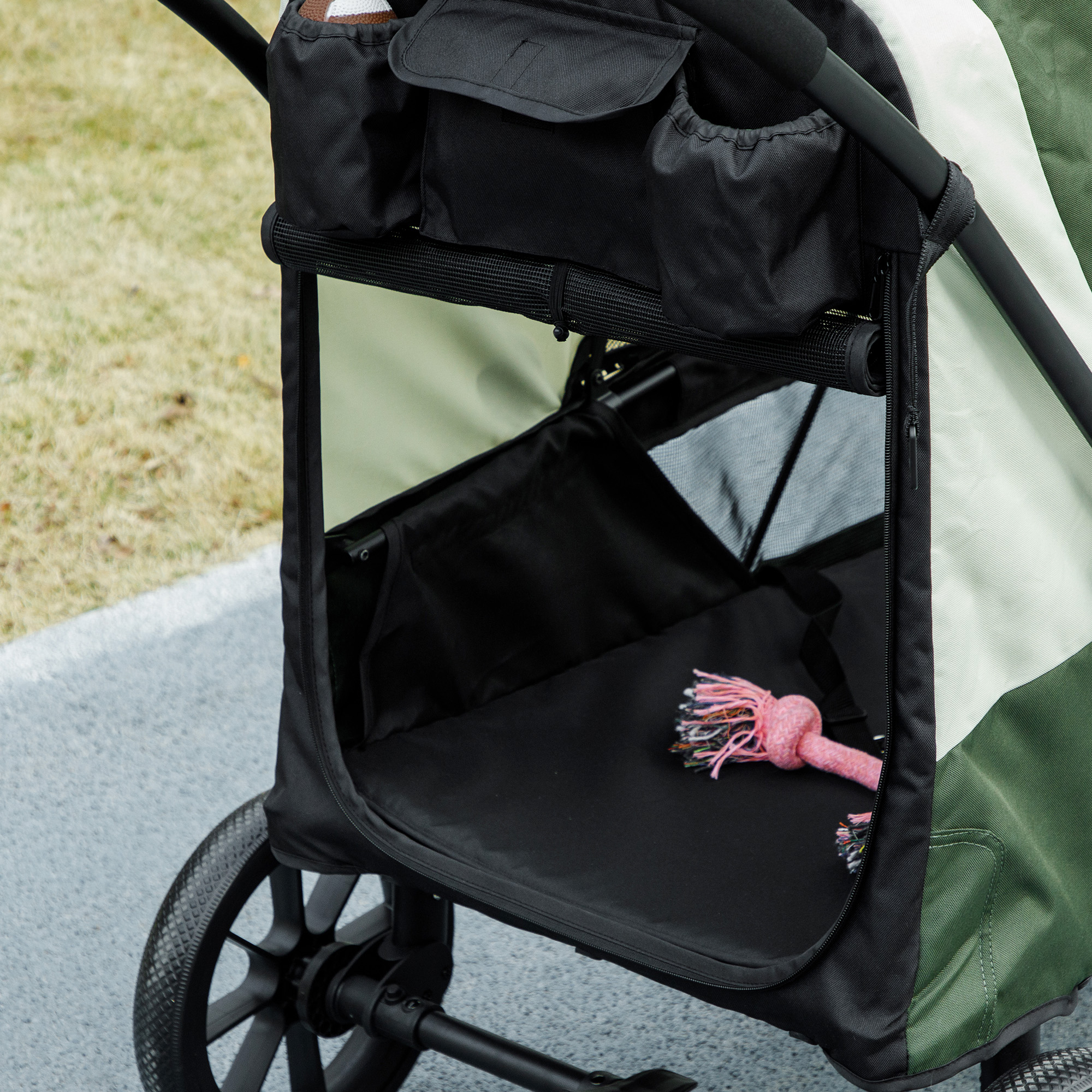 Ein schwarz-grüner Haustierwagen mit einem Hundespielzeug darin. Der Wagen hat Taschen und ein Netzfenster.