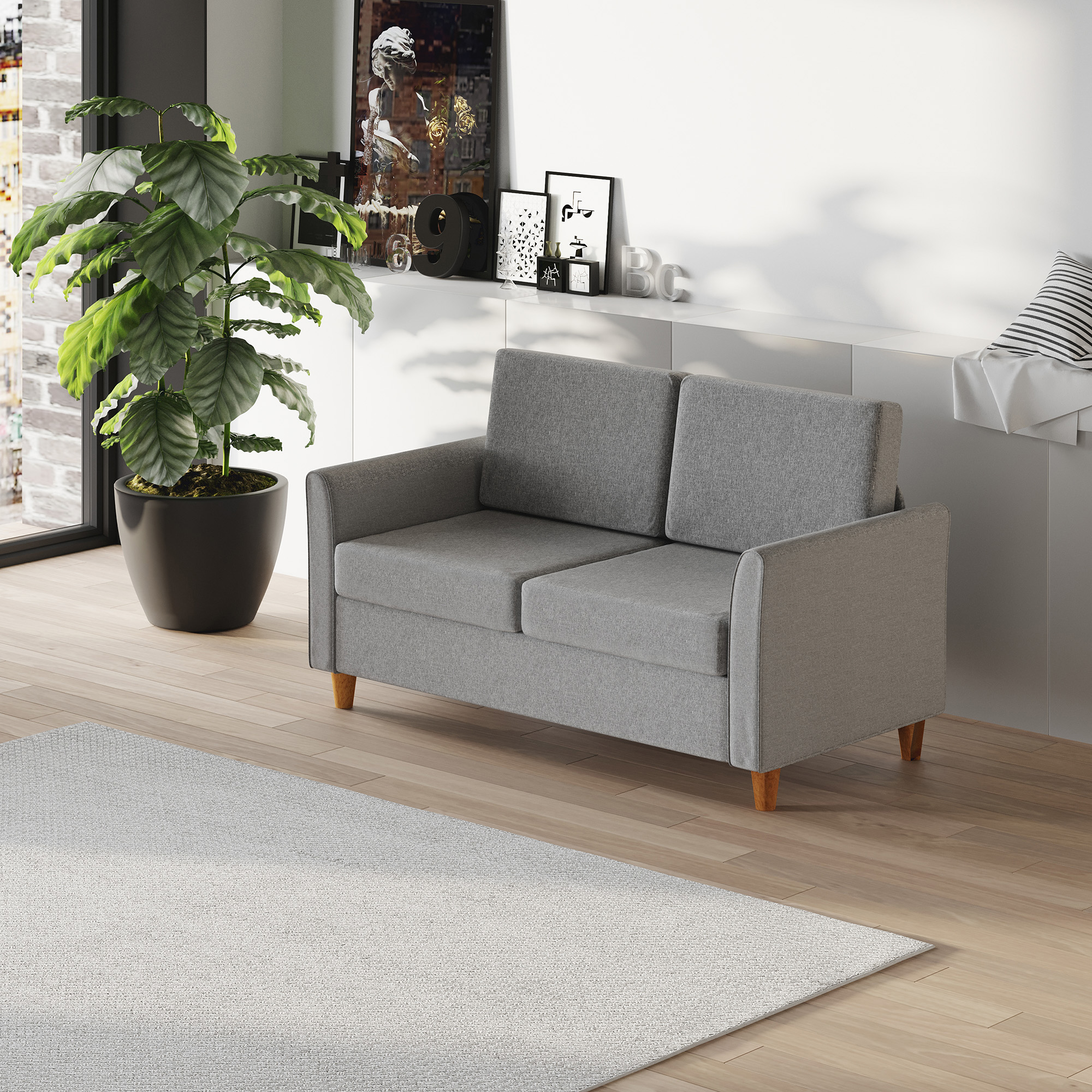Ein graues Sofa mit Holzbeinen vor einer weißen Wand mit Kunst und einer Pflanze.