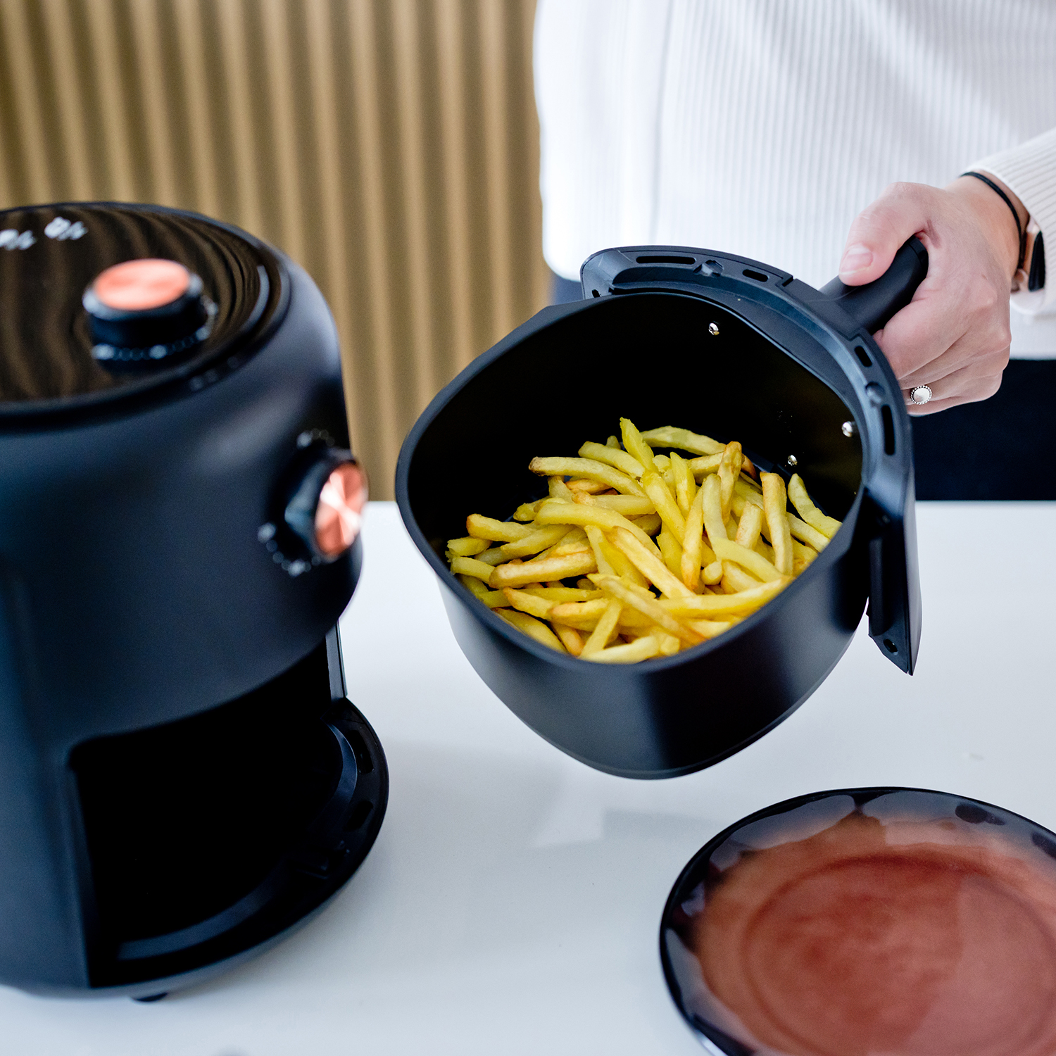 Person hält einen schwarzen Luftfritteusenkorb voller Pommes Frites.