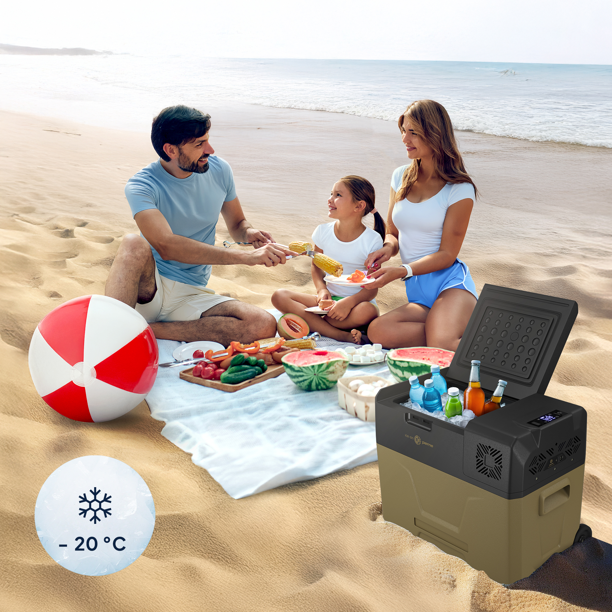 Familie am Strand, mit Kühler, Strandball und Essen auf einer Decke.