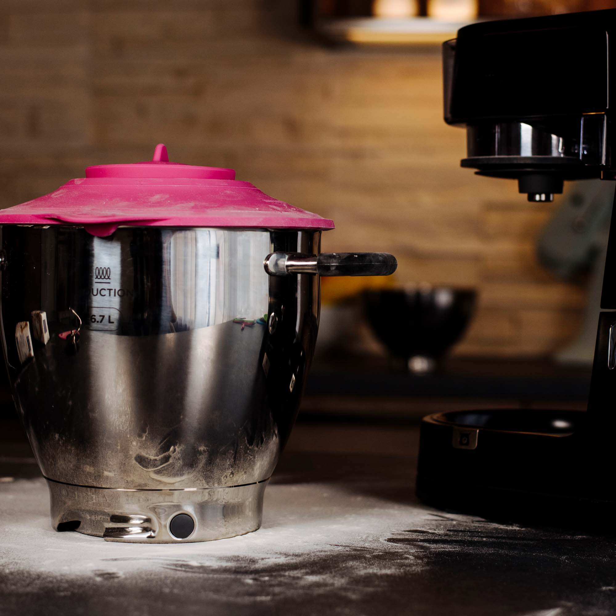 Eine Edelstahl-Mixschüssel mit pinkfarbenem Deckel. Im Hintergrund eine Kaffeemaschine.