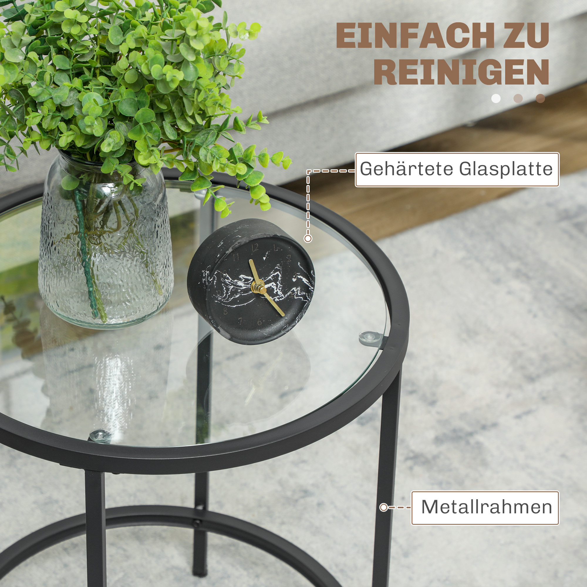 Ein runder Glastisch mit schwarzem Rahmen, eine Uhr und eine Vase mit grünen Pflanzen.
