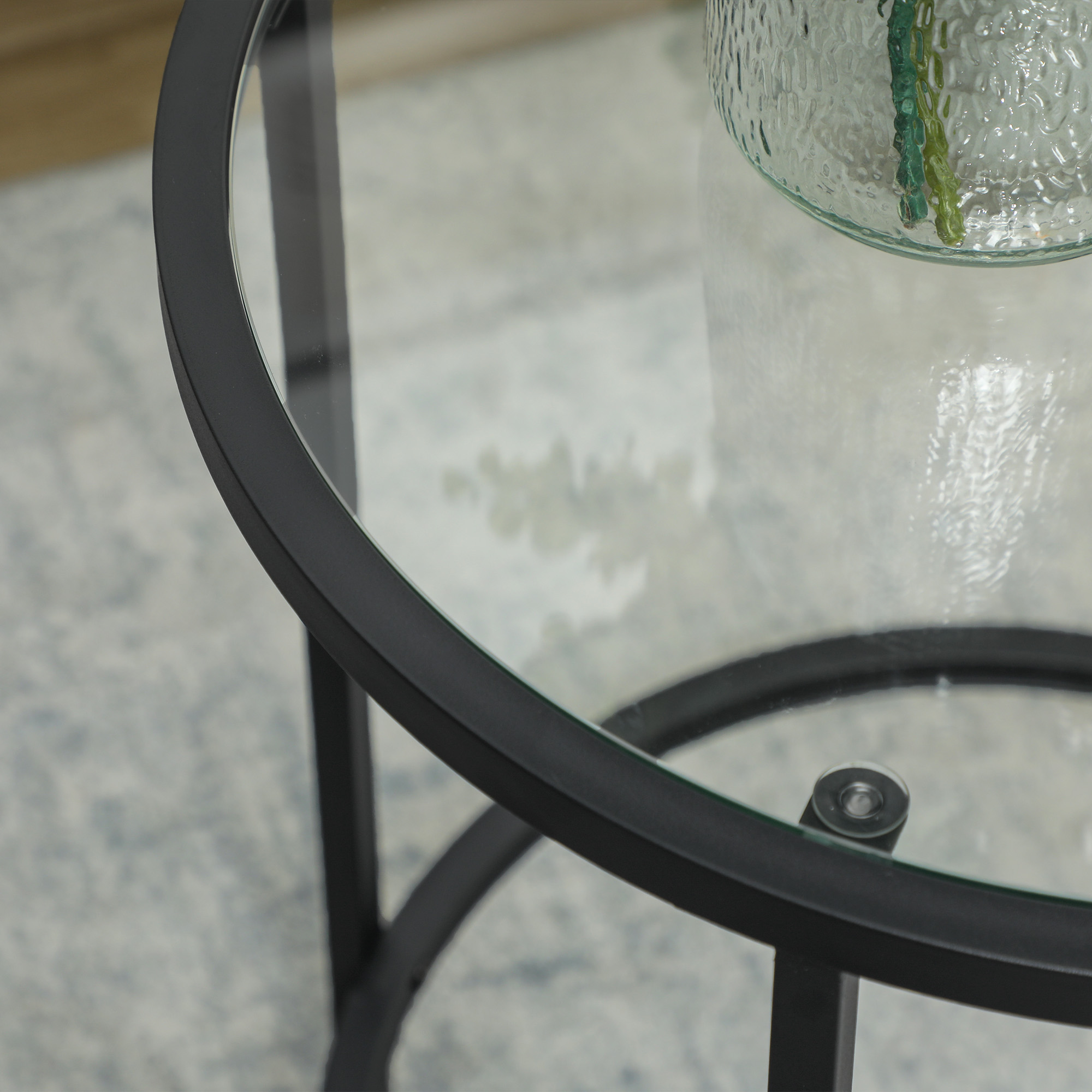 Nahaufnahme eines schwarzen Metalltisches mit Glasplatte. Auf dem Tisch steht eine Vase mit grünen Stielen.