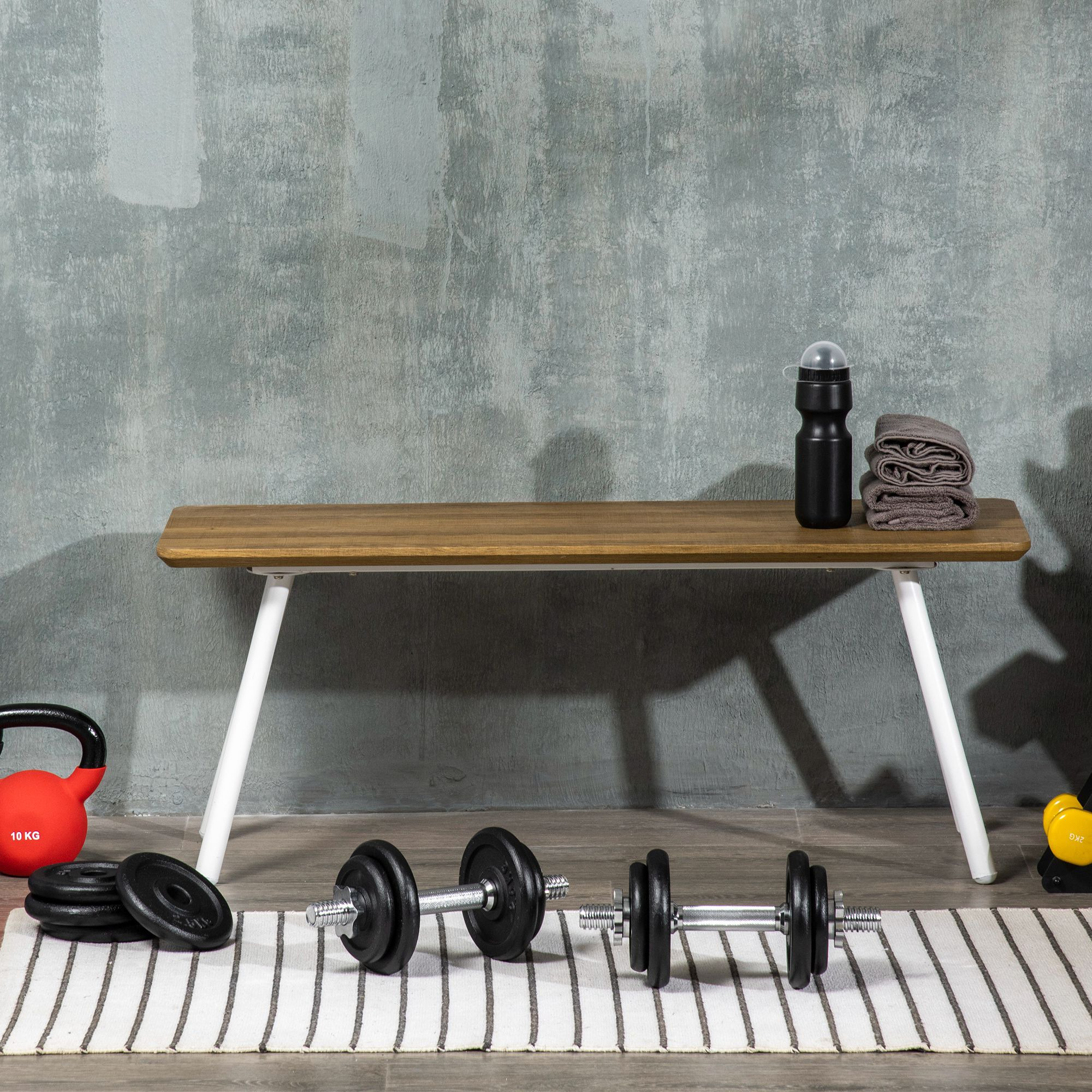 Hantelbank mit Gewichten, Kurzhanteln, einer Kettlebell, einem Handtuch und einer Wasserflasche.