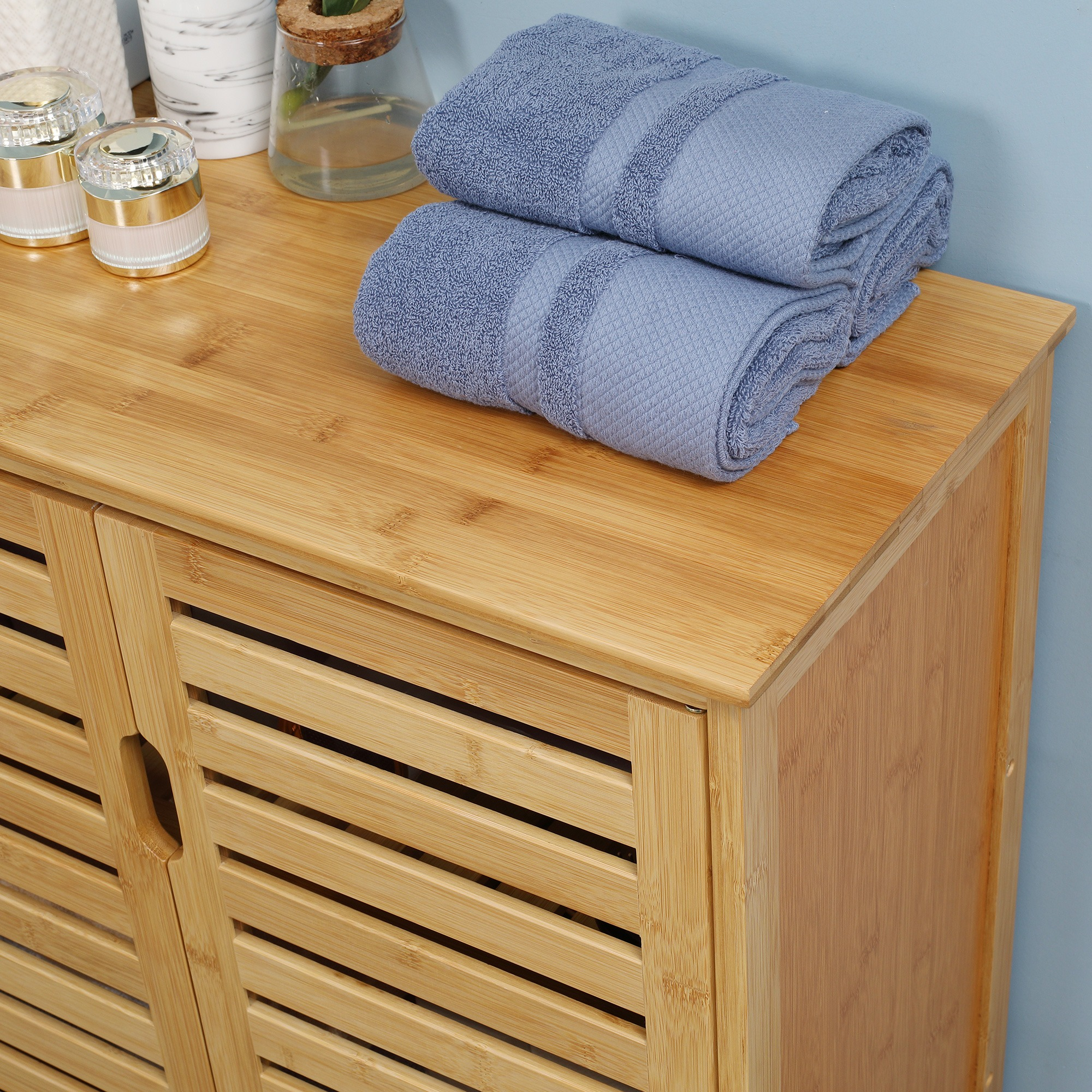 Holzschrank mit Lamellentüren, zwei blaue Handtücher oben und verschiedene Toilettenartikel.