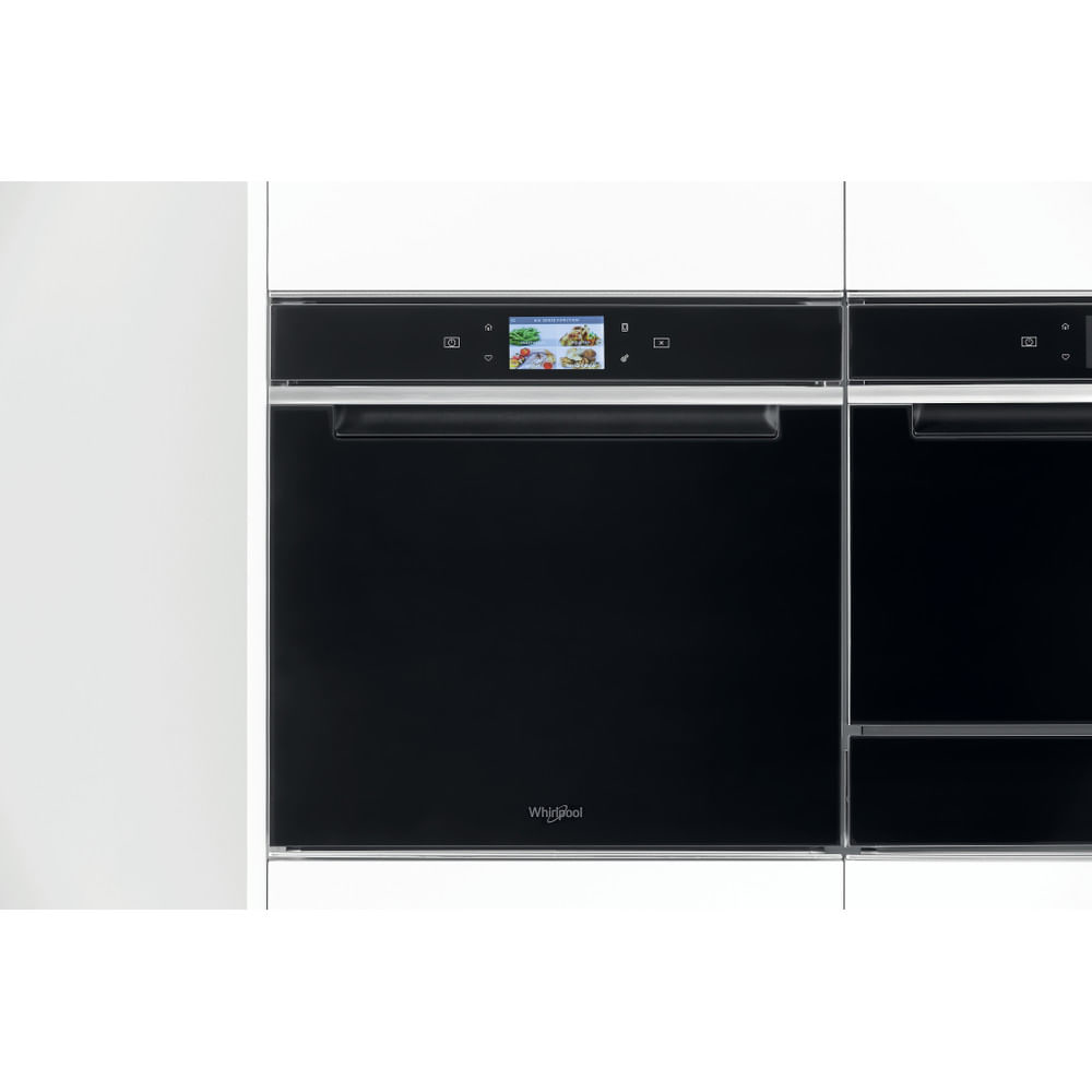 Forno nero con display touchscreen e armadi bianchi ai lati.