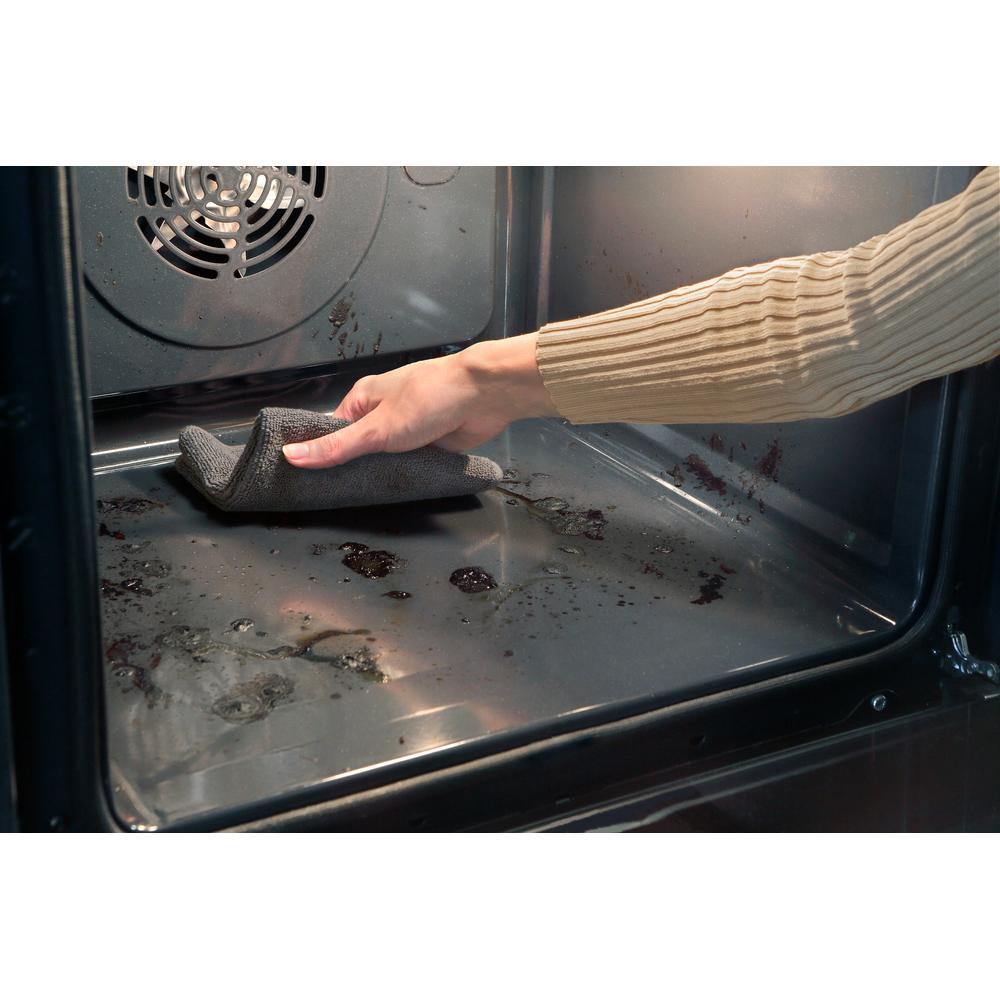Mano limpiando el interior sucio del horno con un paño gris. Grasa y residuos de comida visibles.